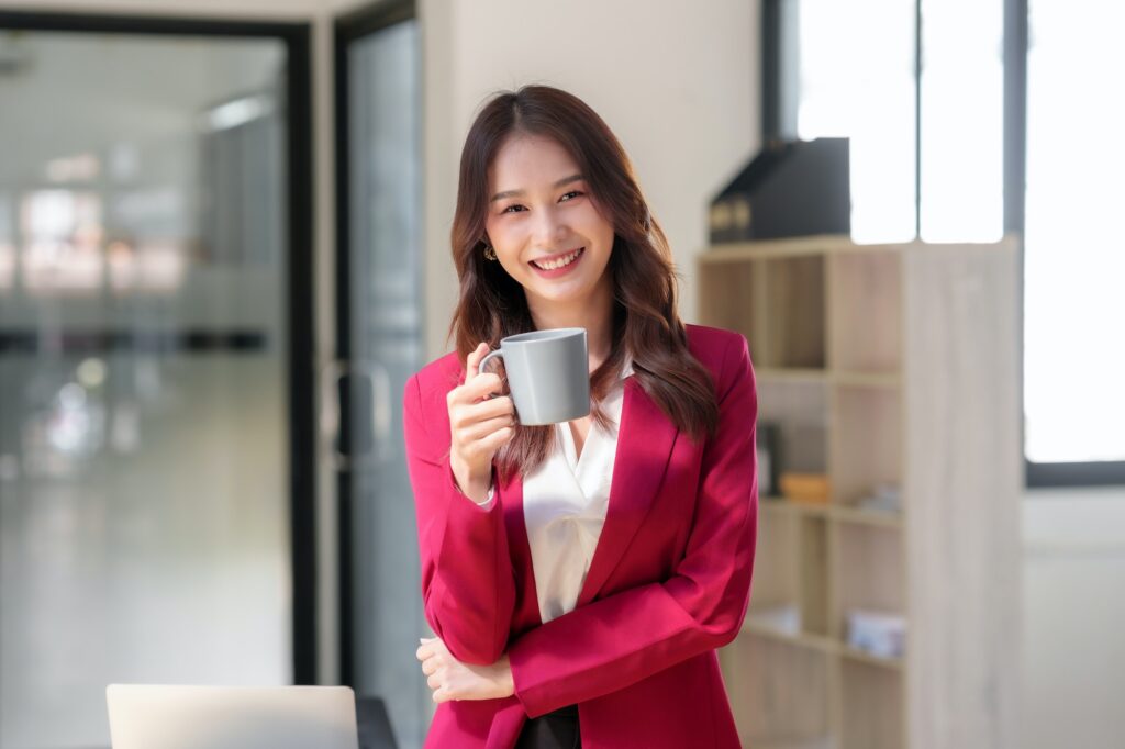 Beautiful Asian business woman standing holding coffee reviewing work and finding new idea
