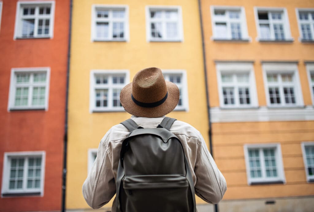 Rear view of senior man tourist outdoors looking at apartment building