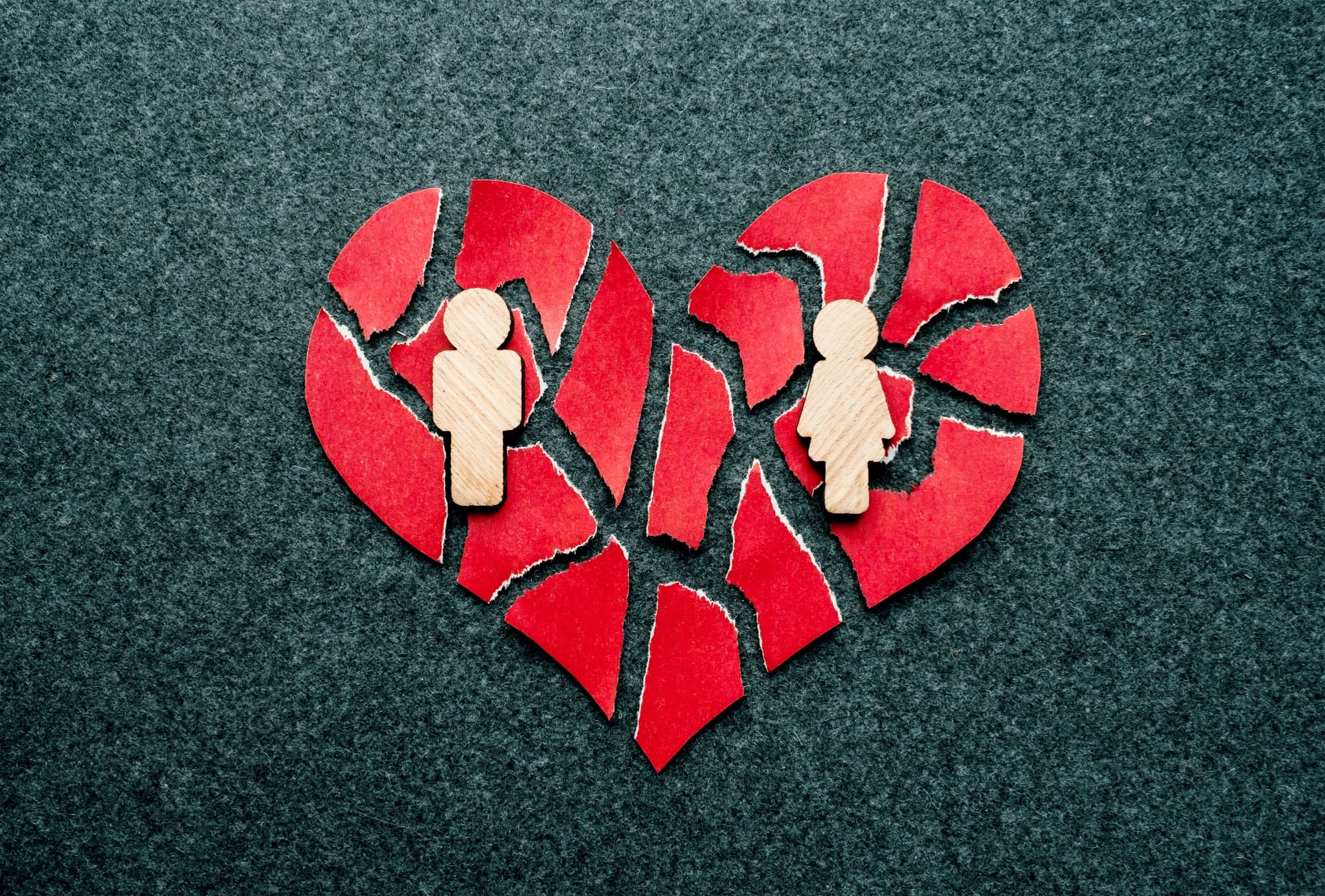 Paper red broken heart with wooden figures of man and woman on dark felt background. Mosaic paper